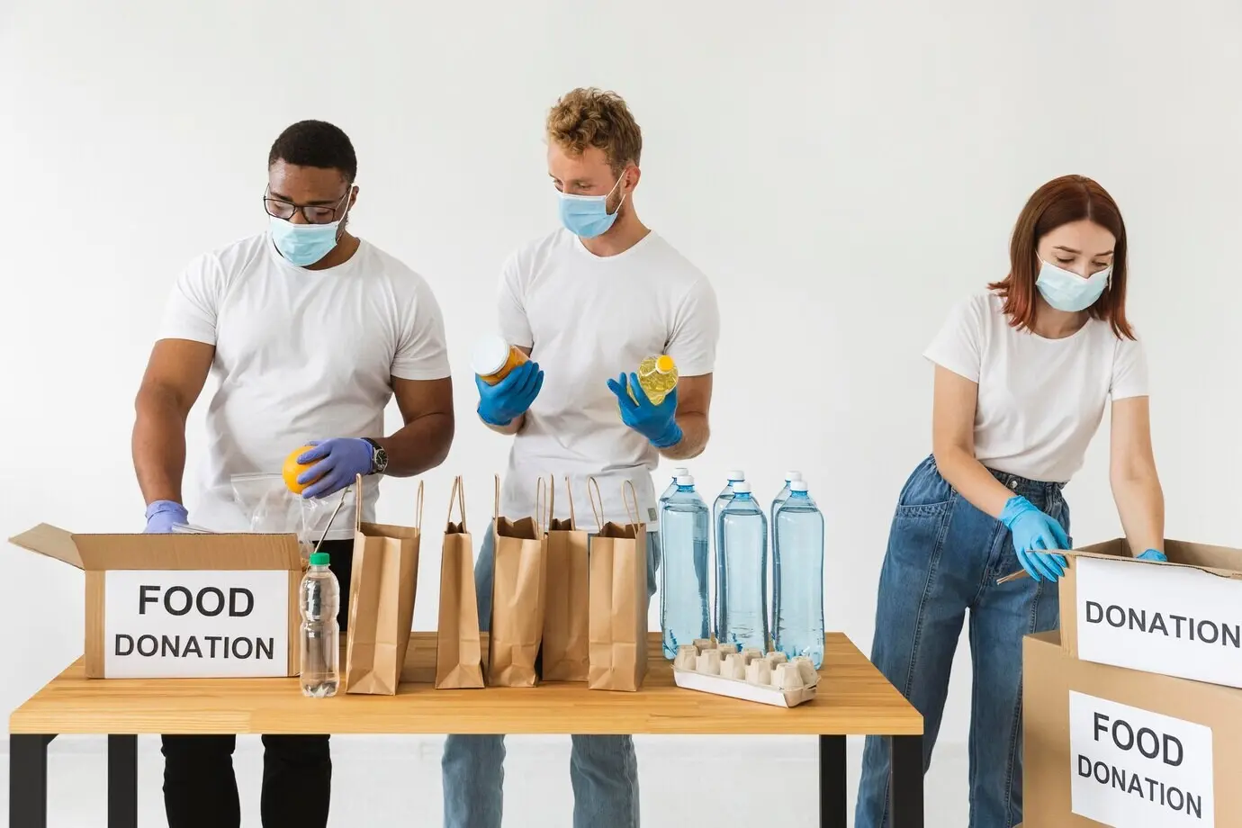 Volunteers wearing gloves and medical masks prepare food for donation with boxes.